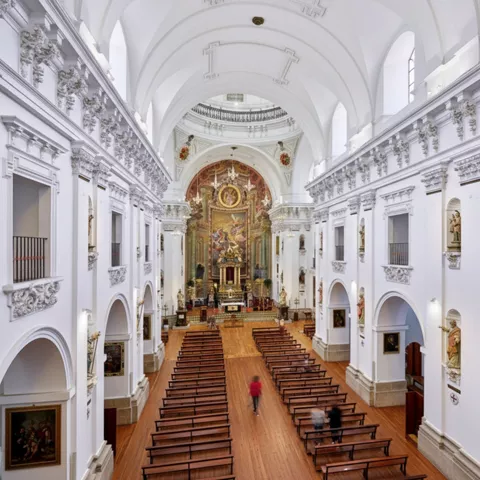 Interior de iglesia barroca con nave alta y retablo al fondo.