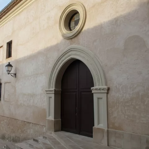 Fachada lateral con portada clásica y viviendas antiguas alrededor.