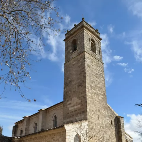 Torre campanario de piedra junto a fachada lateral.