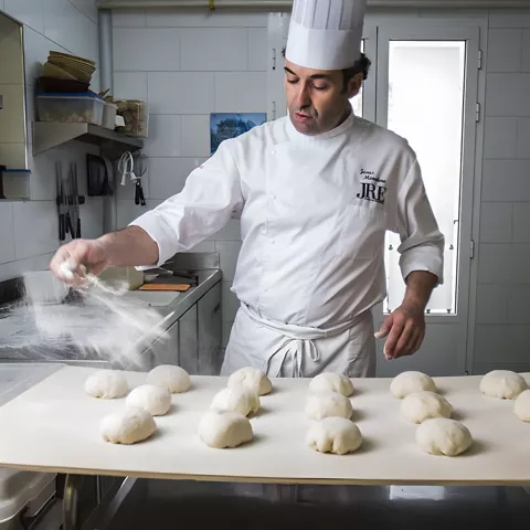 Cocinero espolvoreando harina sobre porciones de masa