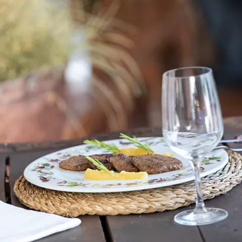 Plato de carne sobre mesa de madera con copa de vino