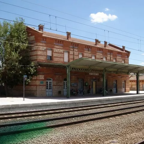 Estación de tren de La Gineta con edificio histórico de ladrillo y andenes junto a las vías.