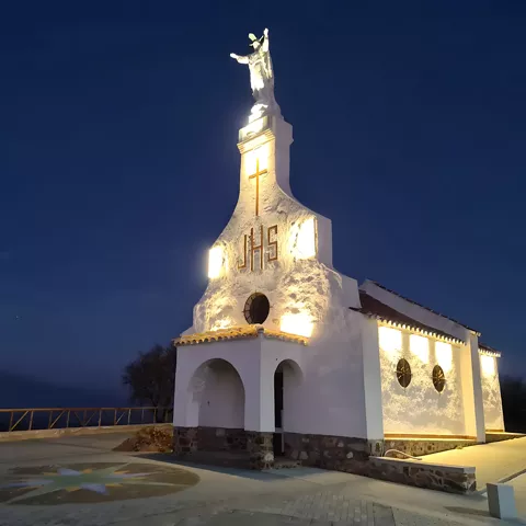 Ermita blanca iluminada de noche con estatua en la fachada