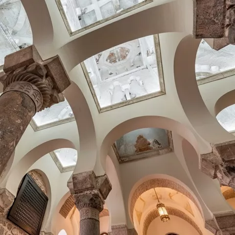 Detalle interior de columnas y arcos blancos bajo techos abovedados.