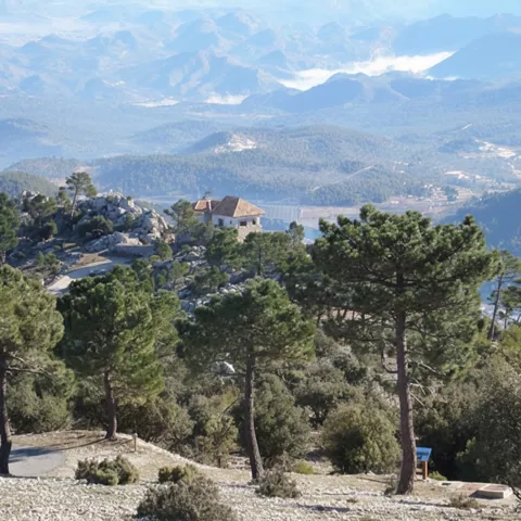 Mirador con pinos y una pequeña construcción sobre un paisaje de montañas y embalse.