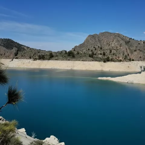 Embalse de agua azul intenso rodeado de montañas rocosas bajo cielo despejado.