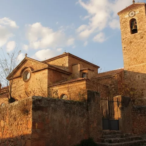 Iglesia de piedra rodeada de árboles y zona ajardinada.