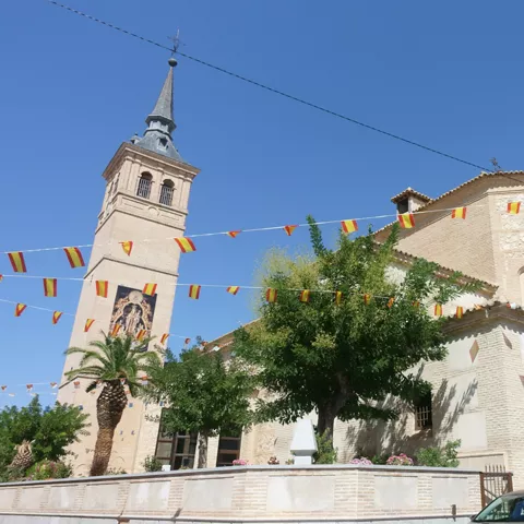 Iglesia de ladrillo con alta torre, banderines y coches aparcados