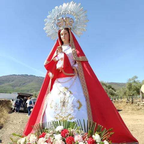Imagen religiosa vestida de rojo y blanco con flores al pie