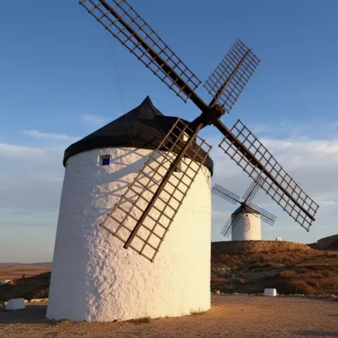 Primer plano de molino blanco con aspas de madera bajo cielo azul.
