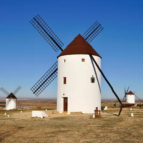 Molino de viento tradicional con aspas negras en paisaje rural despejado.