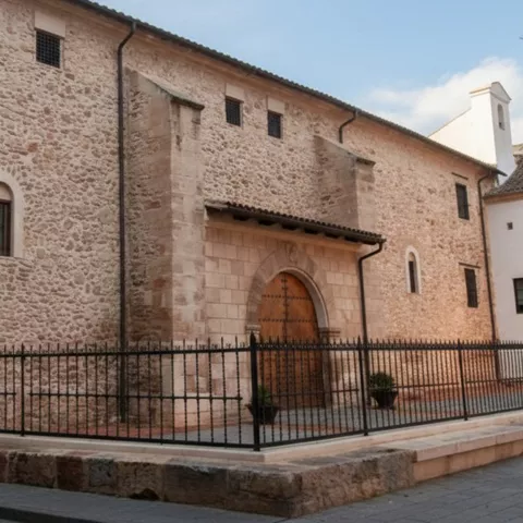 Fachada de piedra con gran puerta de madera y verja metálica en una esquina de calle.