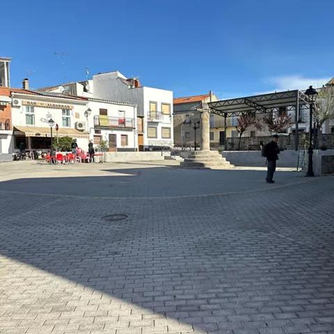 Plaza amplia con terraza de bar, columna de piedra y escenario cubierto