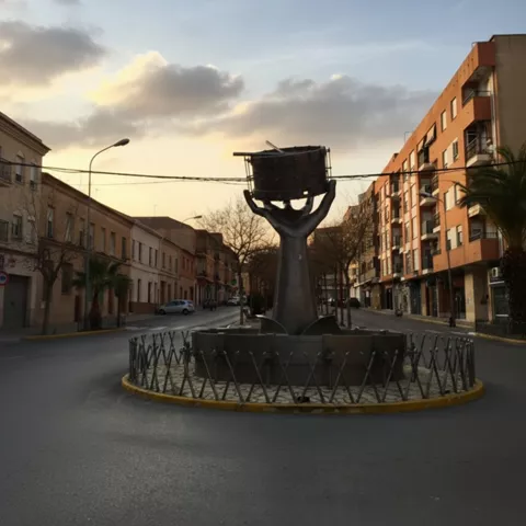 Escultura en rotonda al atardecer, con calles vacías y edificios a ambos lados.