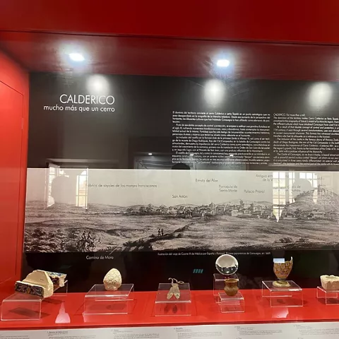 Panel expositivo con ilustración panorámica histórica y piezas arqueológicas en vitrinas rojas.