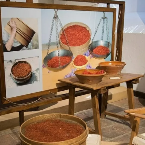 Panel expositivo con balanzas y cuencos llenos de hebras rojas.