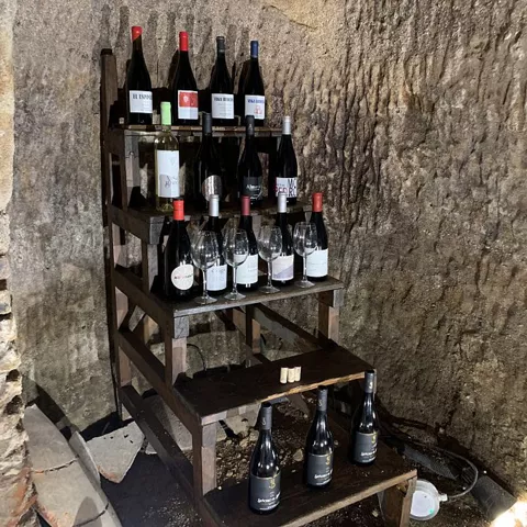 Estantería de madera con botellas y copas en espacio de bodega excavada.