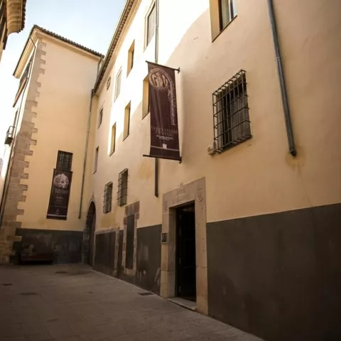 Fachada de museo en calle peatonal con banderolas colgadas.