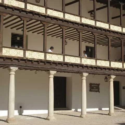 Fachada con soportales y columnas de piedra, con balcones de madera en dos alturas.