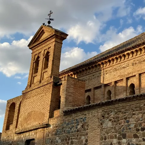 Torre y muro de ladrillo con arcos decorativos bajo cielo parcialmente nublado.