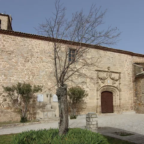Iglesia de piedra con portada ornamental y plaza arbolada