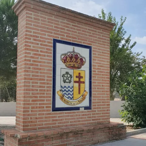 Muro de ladrillo con escudo cerámico en una zona ajardinada