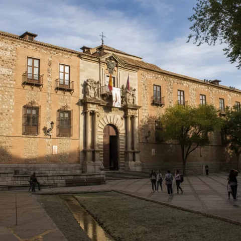 Plaza frente a edificio histórico con estanque rectangular y visitantes.