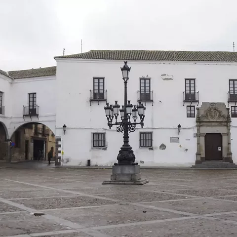 Edificio histórico blanco frente a plaza con farola de hierro