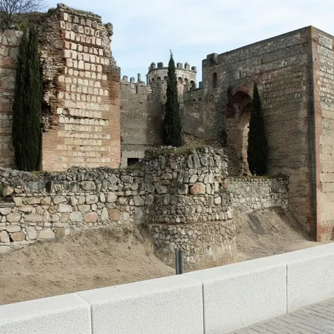 Puerta fortificada y murallas de piedra con cipreses