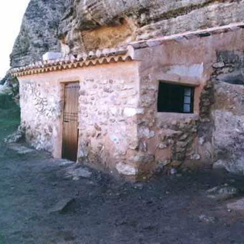 Construcción de piedra integrada en una pared rocosa, con puerta y ventana pequeñas.