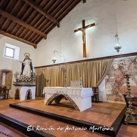 Altar de iglesia con crucifijo, cortina y decoración religiosa sobre paredes de piedra.