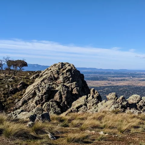Peñas y pastos en altura con vistas abiertas a una gran llanura.