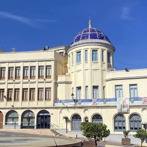 Edificio público de estilo clásico con cúpula azul, balcones y arcos, visto desde la plaza.