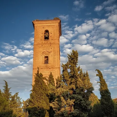 Torre campanario de ladrillo al atardecer con escalinata y cipreses.