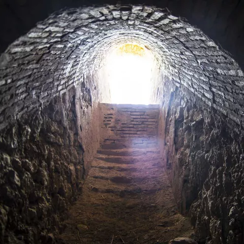 Galería subterránea de ladrillo con luz al fondo.