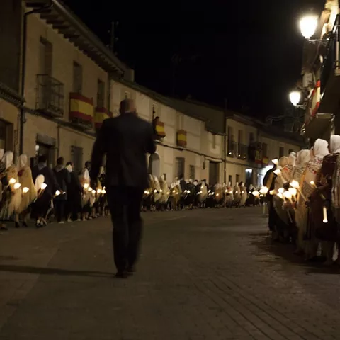 Fila de personas con mantillas y velas encendidas durante una procesión nocturna