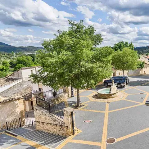 Plaza con fuente central, árboles y edificios de piedra.