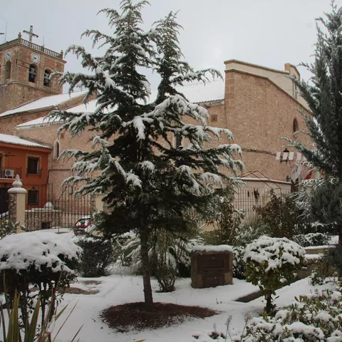 Plaza con jardín y edificio religioso cubiertos de nieve.