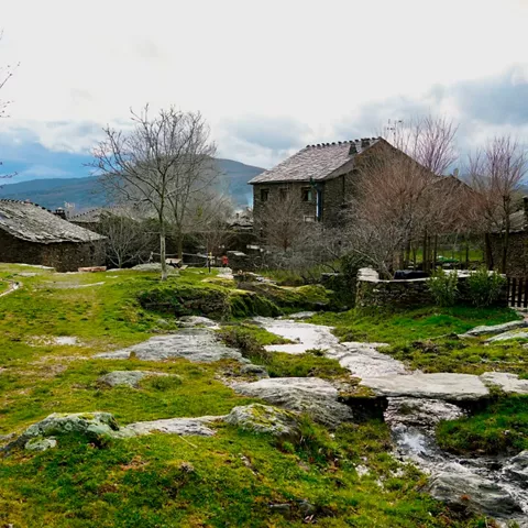Conjunto de casas de piedra junto a un arroyo y pradera.