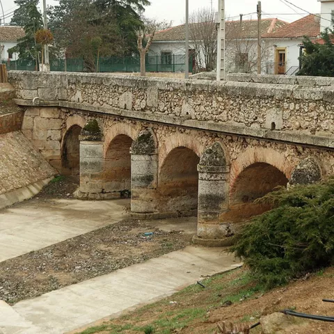 Puente antiguo de piedra con arcos sobre cauce seco.