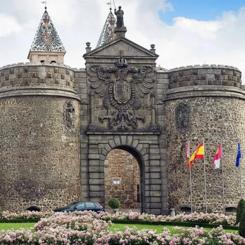 Puerta monumental de piedra con torres circulares y jardín en rotonda.
