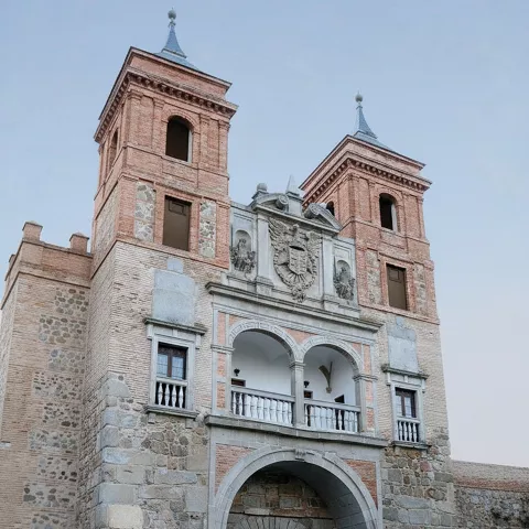 Fachada fortificada con balcón y escudo tallado bajo cielo nublado.