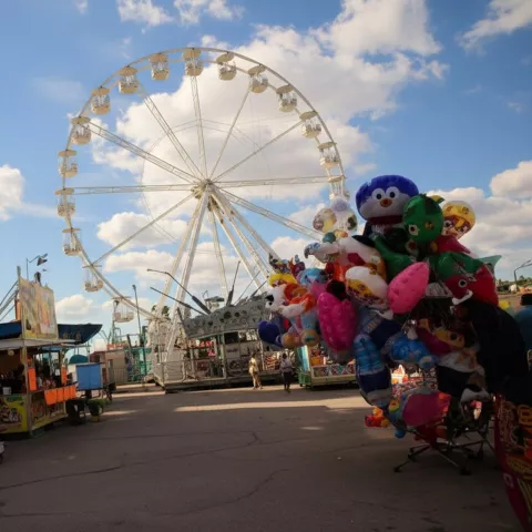 Noria junto a casetas y peluches en una feria al aire libre.
