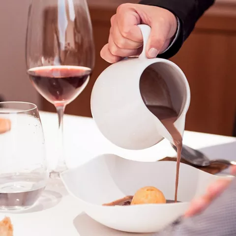 Mano sirviendo salsa sobre un plato blanco en una mesa de restaurante.
