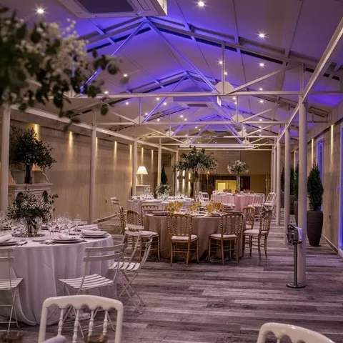 Salón de celebraciones con iluminación ambiental y mesas vestidas.