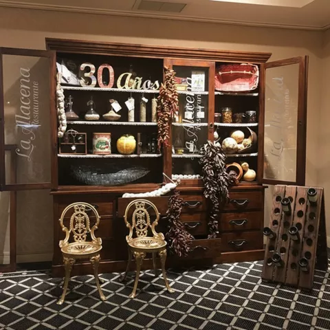 Aparador de madera con objetos decorativos, sillas doradas y botellero.