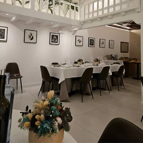 Salón luminoso con techo acristalado, plantas en galería superior y mesa grande preparada.