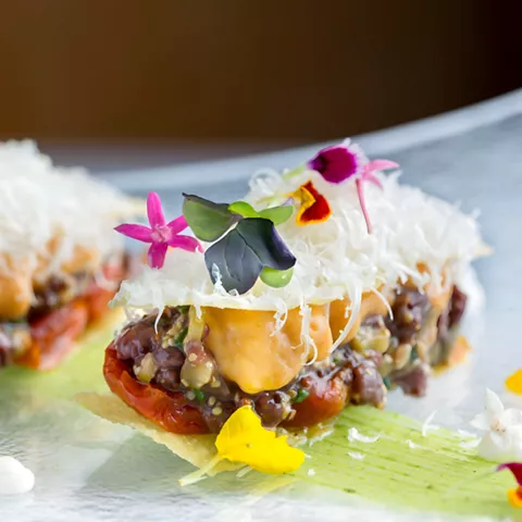 Tapa gourmet con flores comestibles sobre plato de cristal