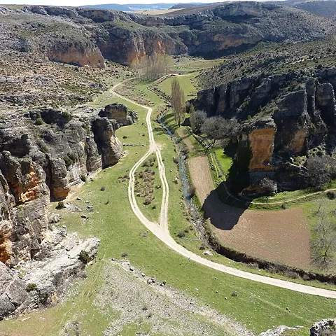 Valle rocoso con camino de tierra y arroyo entre paredes escarpadas.