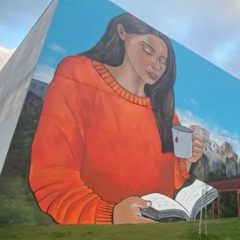 Gran mural de mujer leyendo y sosteniendo una taza en edificio moderno.